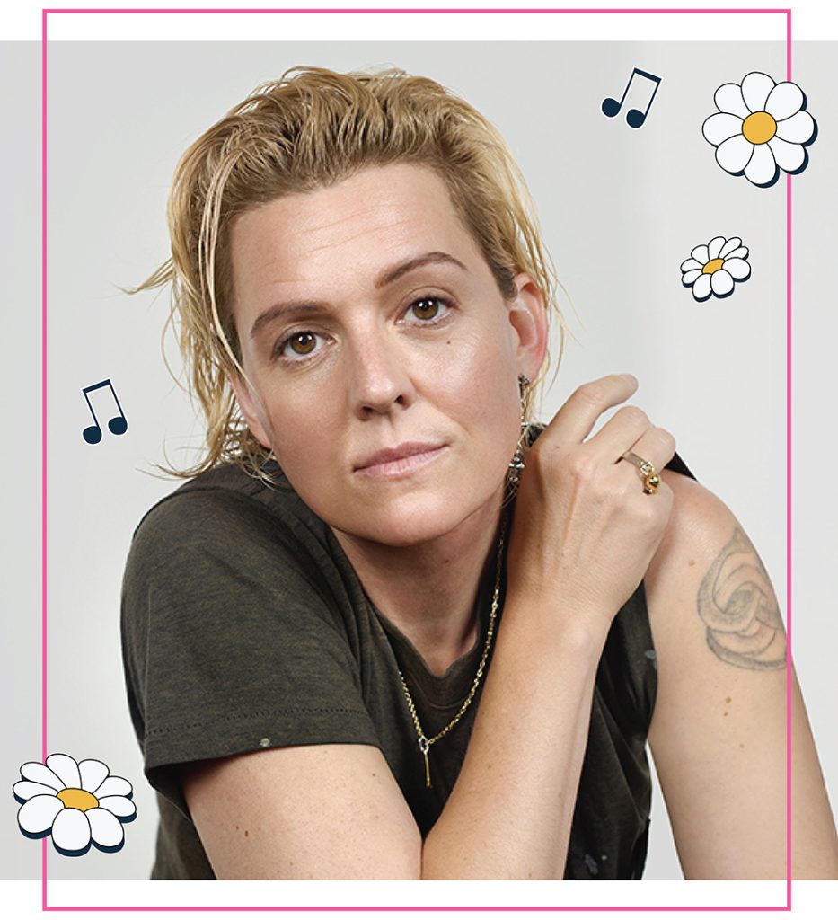 Photo of Brandi Carlile in a dark t-shirt with a tattoo on her arm, framed with a pink border and daisy and music note illustrations.